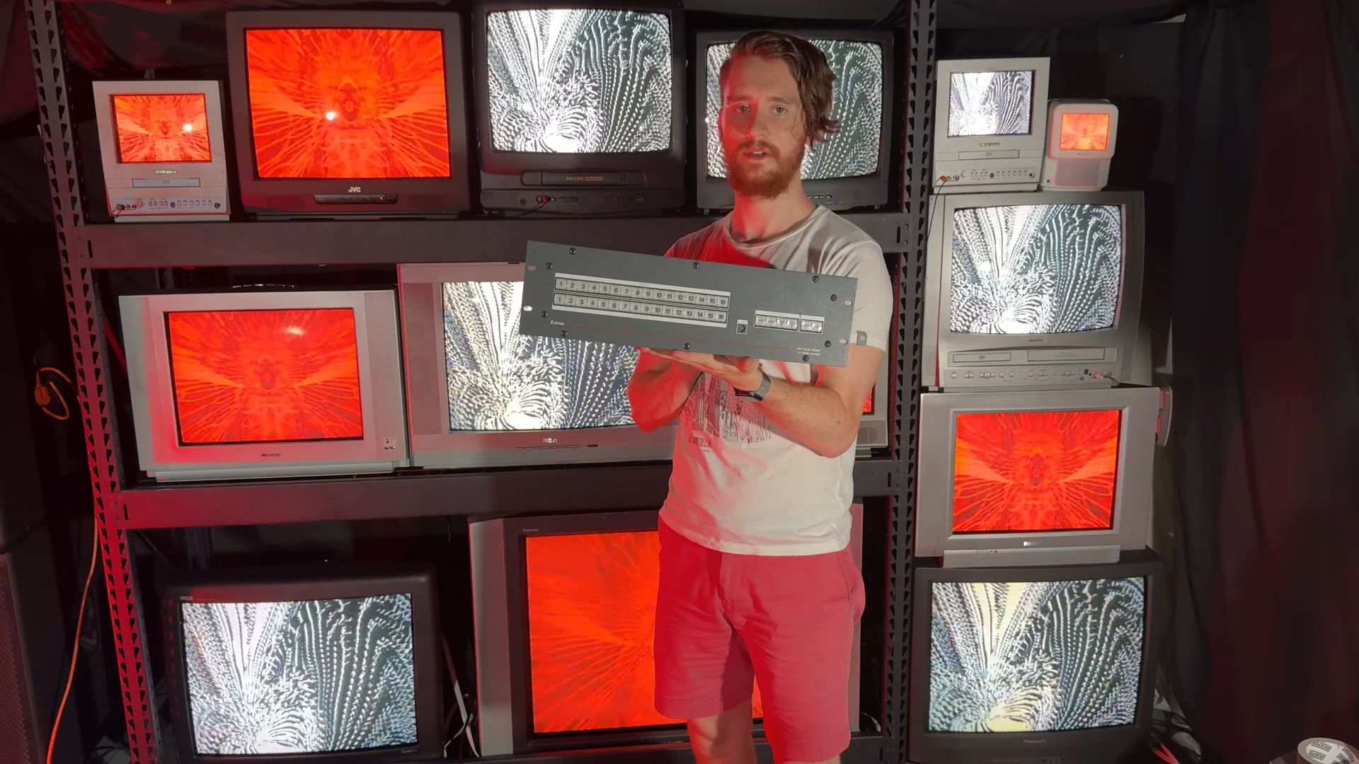 Tom is holding the Extron matrix switcher in front of the CRT TV wall displaying real-time visual effects.