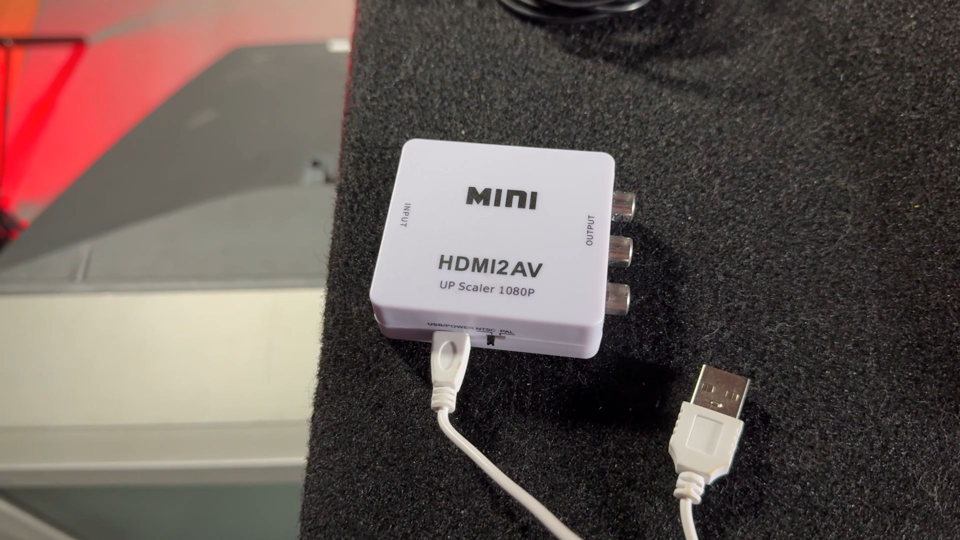 A mini HDMI to AV converter labeled "HDMI2AV" with input, output, and USB power connectors, placed on a table.