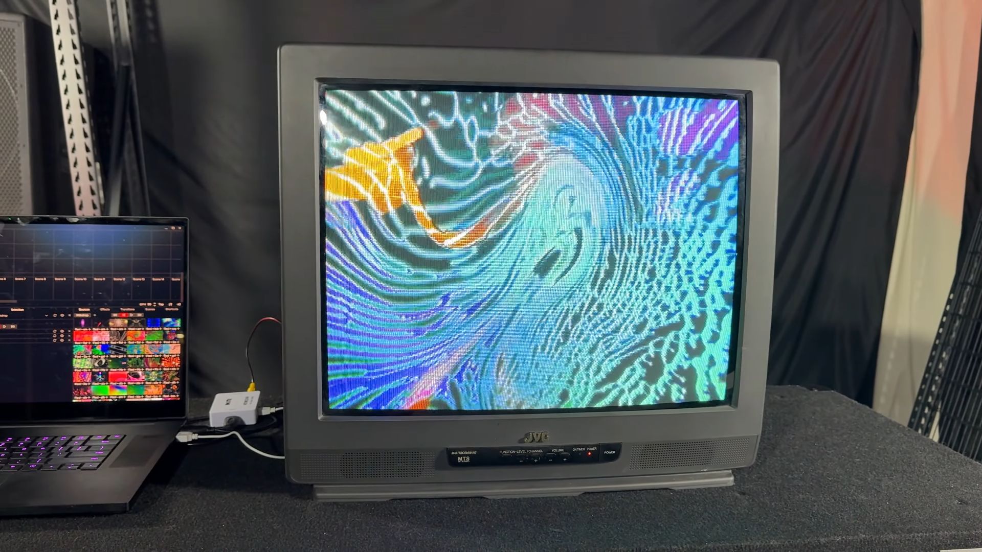 A vintage JVC CRT television displaying colorful abstract graphics, connected to a modern laptop via an HDMI to AV converter.