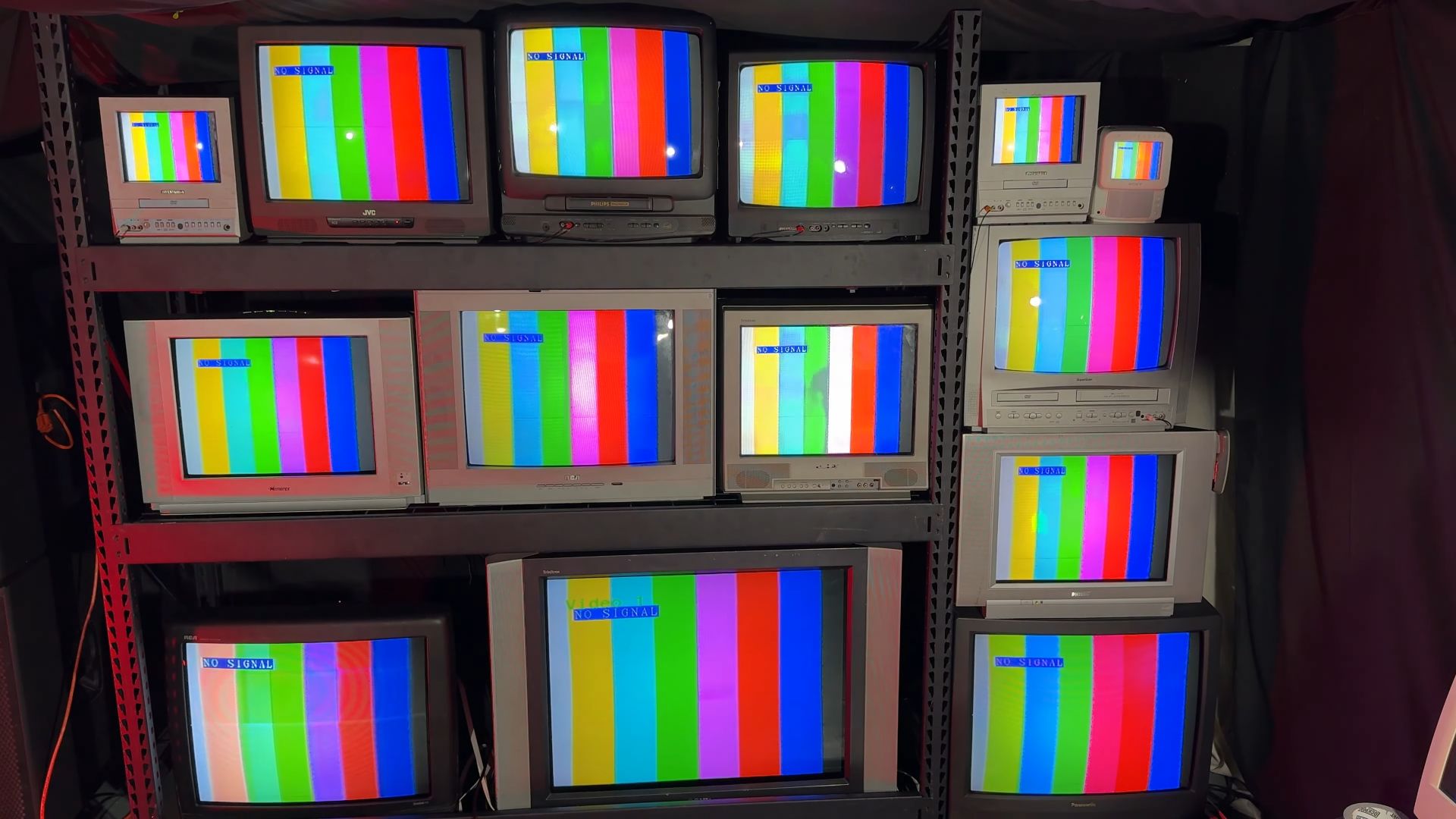 Multiple CRT monitors on a steel shelf, displaying color bars and "NO SIGNAL" text.