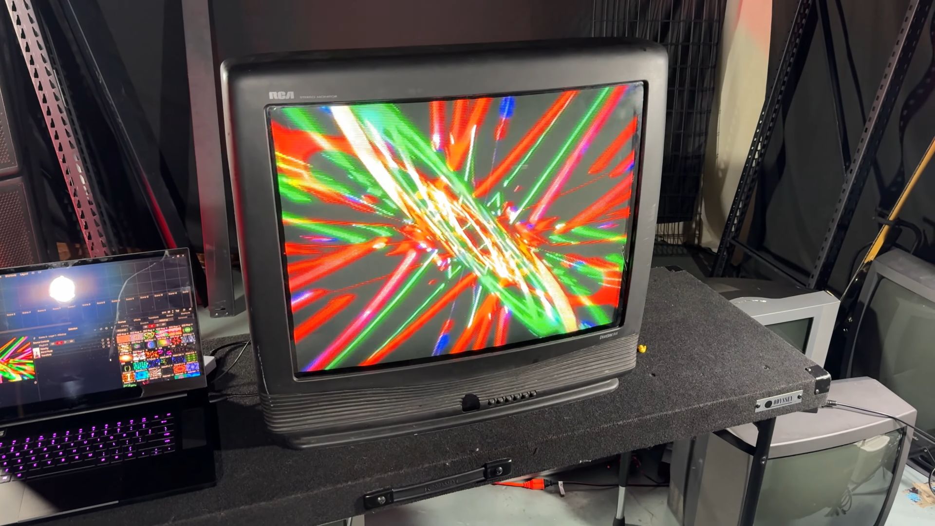 A large, heavy RCA CRT television displaying colorful abstract graphics, connected to a laptop running Nuvotion visuals software on a table.