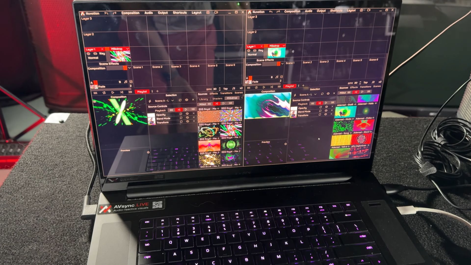 A laptop running Nuvotion visuals software, displaying various scenes and effects in a grid layout. The screen shows different colorful abstract graphics being edited.