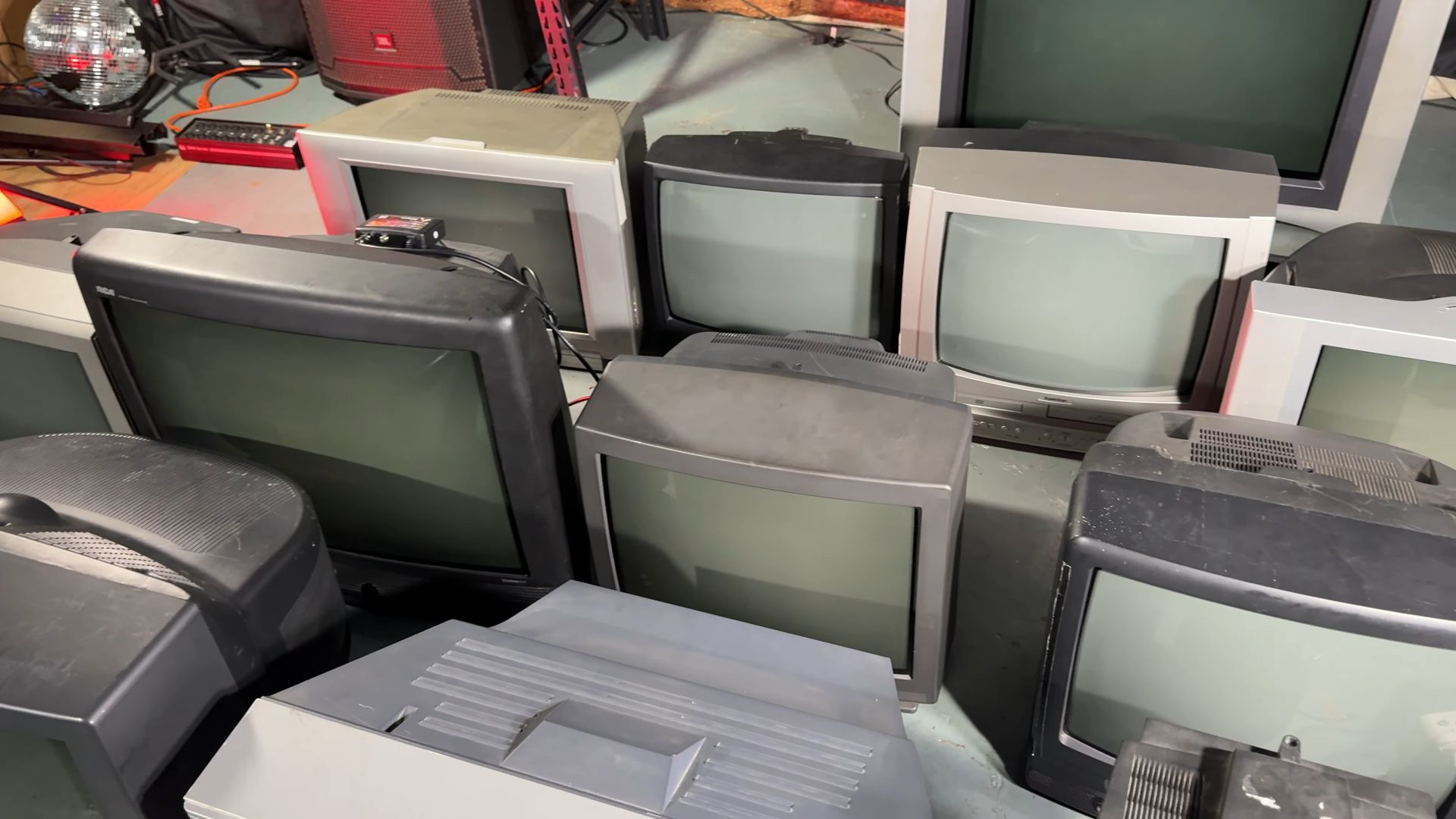 A collection of vintage CRT televisions arranged on a basement floor, displaying their large screens and bulky designs.