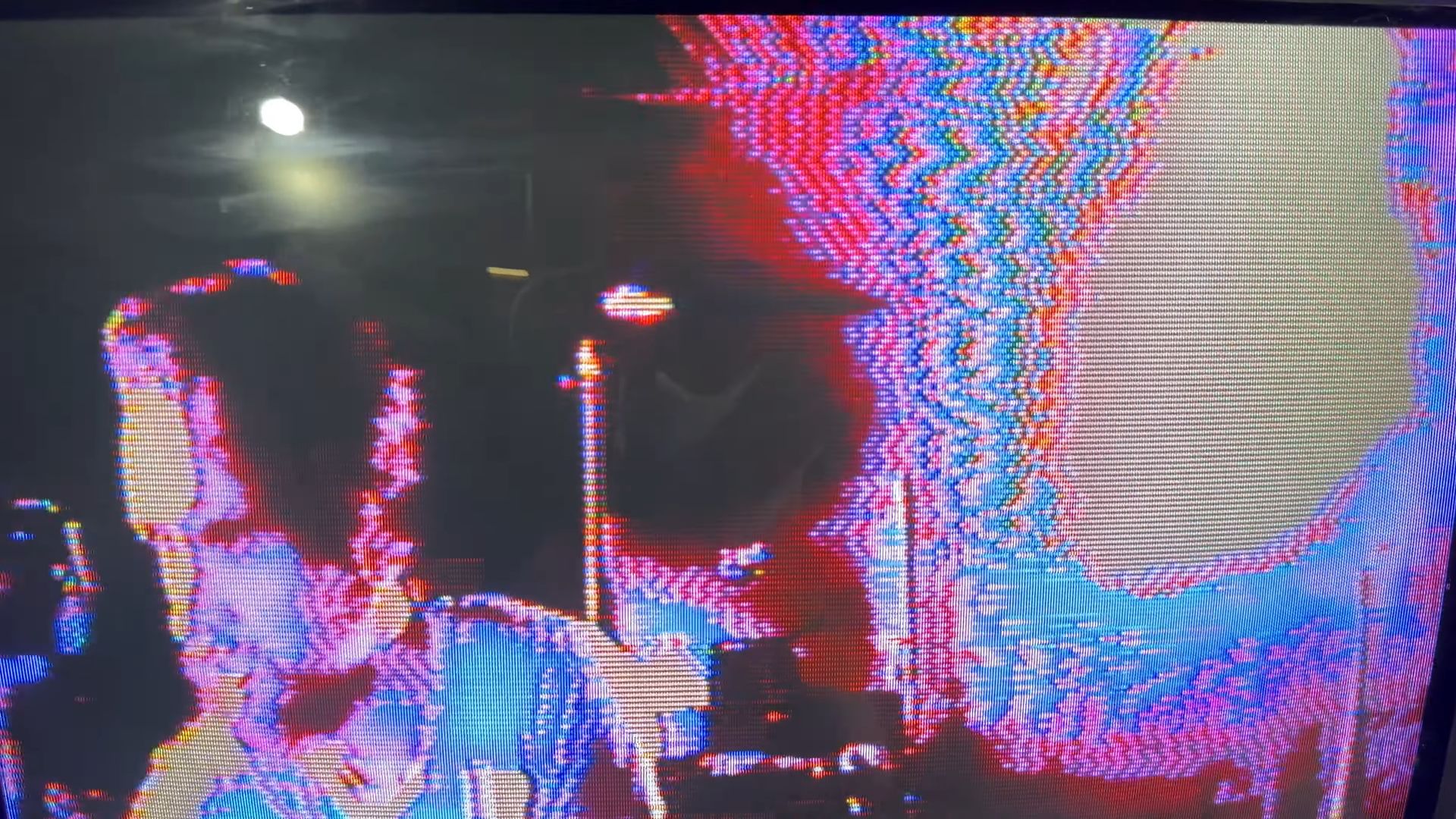 A close-up of a vintage CRT television screen displaying a distorted, colorful image of Tom.