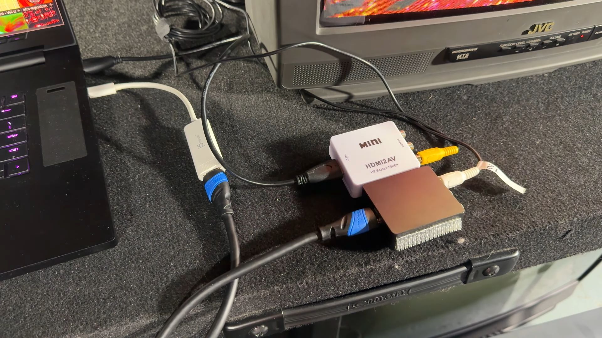 A setup with two HDMI to AV converters on a table, connected to a laptop and a vintage CRT television displaying colorful graphics.